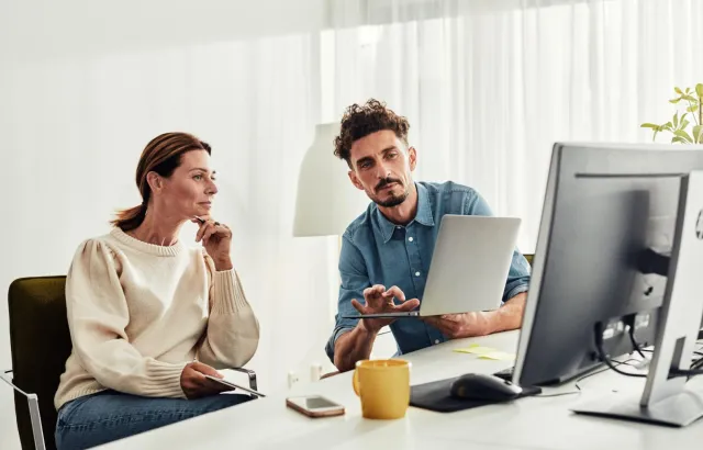 Person showing woman something on their laptop, at a desk