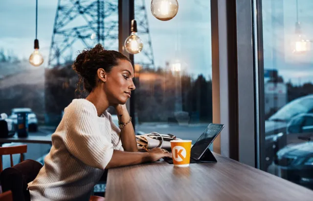 Woman relaxing on her tablet by large windows in a Circle K café, with a coffee