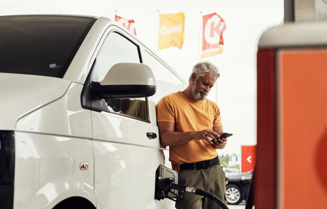 Man looking at something on his phone, while leaning against his van, while it is being fueled